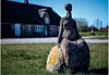 Steinfigur auf einer Wiese vor einem Backsteinhaus mit Reetdach