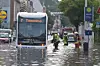 Überflutete Straße mit Feuerwehrleuten neben einem stehenden Linienbus vor Stadtgebäuden