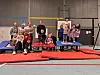 Gruppe aus Kindern und Erwachsenen auf Trampolinen und roten Turnmatten in einer Sporthalle