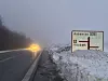 Verschneite Straße bei Nebel mit Straßenschild nach Aabenraa und Scheinwerfern eines Autos