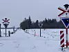 Verschneiter unbeschrankter Bahnübergang mit Warnschildern in winterlicher Landschaft.