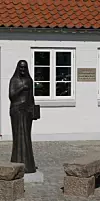 Bronzestatue einer Frau vor weißem Haus mit Sprossenfenstern