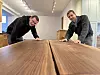 Zwei Männer beugen sich in einem Showroom über eine große Massivholzplatte.
