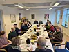 Menschen sitzen zum Frühstück an einem langen Tisch in einem hellen Versammlungsraum.