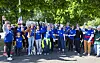 Gruppe von Frauen in blauen T-Shirts jubelt gemeinsam im Freien unter grünen Bäumen.