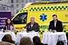Drei Vertreter von Moderaterne halten vor einem gelben Falck-Rettungswagen eine Gesundheitspressekonferenz ab.