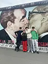 Vier Jugendliche stehen vor dem bemalten Mauerstück mit Kussmotiv an der East Side Gallery.