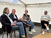 Vier Personen sitzen in einem Zelt im Stuhlkreis und führen ein Gespräch.