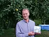Mann steht vor Apfelbaum und zeigt eine kleine Produktverpackung