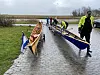 Mehrere Ruderer ziehen zwei Ruderboote auf Wagen über einen nassen Weg zum Wasser.