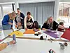 Erwachsene und Kinder sitzen an einem Tisch und basteln mit buntem Papier.