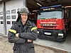 Älterer Feuerwehrmann in Einsatzkleidung steht vor rotem Iveco-Feuerwehrauto vor dem Gerätehaus.