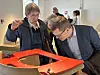 Mehrere Personen beugen sich in einem Museumsraum über ein rotes Holzobjekt.