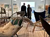 Zwei Personen stehen in einem hellen Ausstellungsraum mit Designstühlen und Bildern an den Wänden.