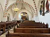 Blick durch das Kirchenschiff mit Holzbänken, bemalten Gewölben und Orgel im Hintergrund.