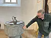 Mann betrachtet ein steinernes Taufbecken mit Metallkanne in einer hellen Kirche.